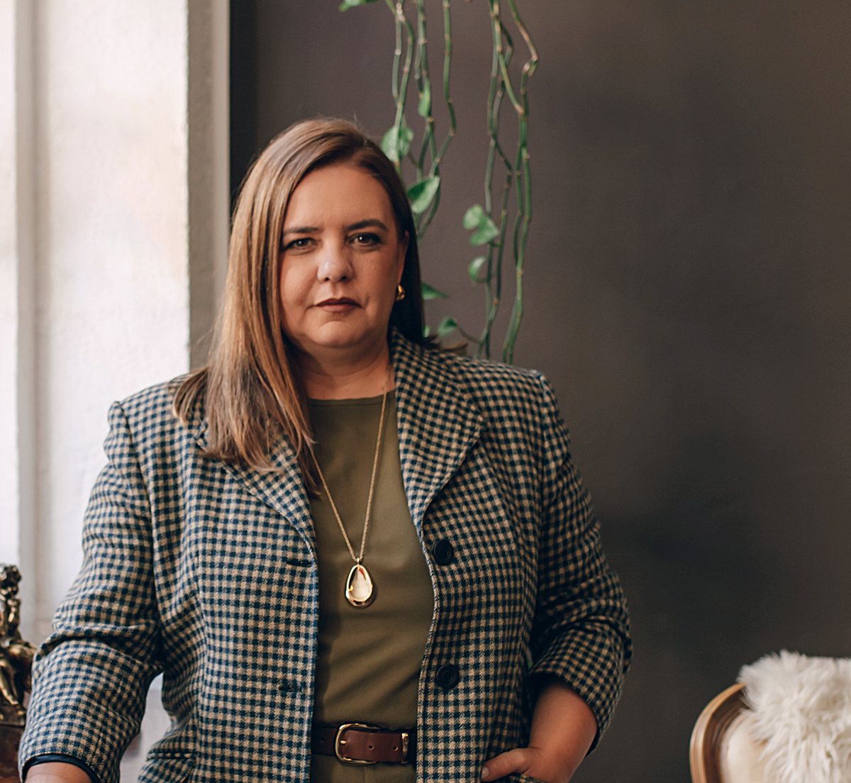 Paula Dias Aguiar, de blazer pied-de-poule sobre conjunto verde-oliva, num interior
